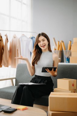 Genç işyeri sahibi kadın paket kutusunu hazırla ve tablet, dizüstü bilgisayar alışverişi online konsept üzerinden müşteriye teslimat için çevrimiçi kontrol yap