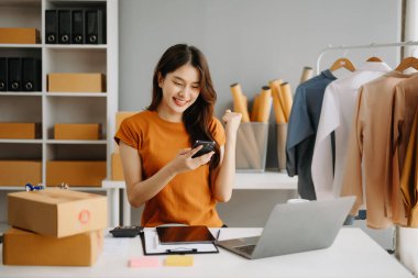 Moda blogcusu kavramı, giysi satan genç Asyalı kadın. Akıllı telefon ve dizüstü bilgisayar kullanarak küçük işletme KOBİ 'si kurun, ofiste satın alın ve kontrol edin