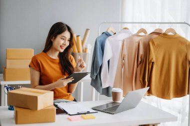 Moda blogcusu kavramı, genç Asyalı kadın video yayınında kıyafet satıyor. Tablet ve dizüstü bilgisayar kullanarak küçük işletme KOBİ 'si kurun.