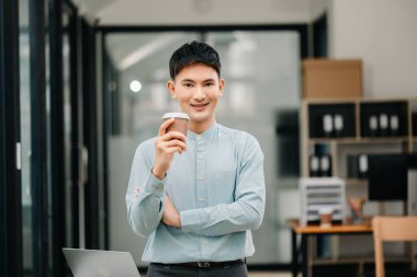 Genç ve çekici Asyalı işadamı modern ofiste kahve içiyor.