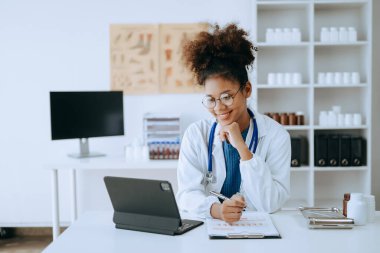 Afrikalı gülümseyen doktor veya danışman bir masada oturmuş hasta raporu, ameliyat planı ve reçete yazıyor.. 