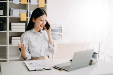 Mutlu Asyalı iş kadını modern ofiste akıllı telefon kullanmaktan zevk alıyor.