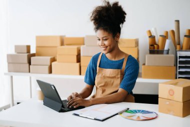 Küçük işletme KOBİ 'si kurun. Girişimci Afrikalı kadın internetten sipariş almak ve kontrol etmek için tablet bilgisayar kullanıyor. Genç bayan küçük işletme sahibi bunları müşterilere göndermek için paket paketliyor.