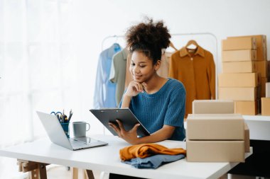 Küçük işletme KOBİ 'si kurun. Girişimci Afrikalı kadın online siparişleri alıyor ve kontrol ediyor. Genç bayan küçük işletme sahibi bunları müşterilere göndermek için paket paketliyor.