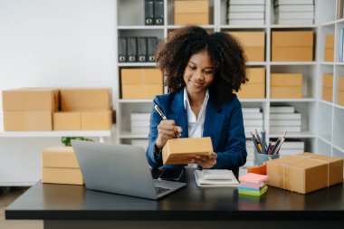 Küçük işletme KOBİ 'si kurun. Girişimci Afrikalı kadın internetten sipariş almak ve kontrol etmek için laptop kullanıyor. Genç bayan küçük işletme sahibi bunları müşterilere göndermek için paket paketliyor.