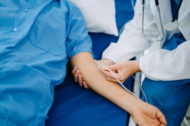 Kadın doktor, hastanede ya da klinikte salin solüsyonu alan yaşlı hasta elini yatağın üzerinde tutuyor.