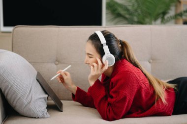 Gülümseyen kız evde dinleniyor, kulaklıkla müzik dinliyor ve oturma odasında dijital tablet kullanıyor.