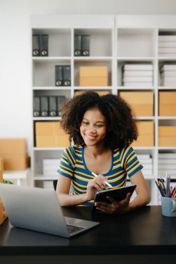 Küçük işletme KOBİ 'si kurun. Girişimci Afrikalı kadın online siparişleri alıyor ve kontrol ediyor. Genç bayan küçük işletme sahibi bunları müşterilere göndermek için paket paketliyor.
