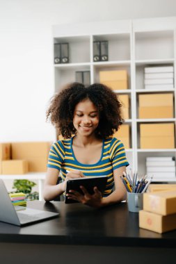 Küçük işletme KOBİ 'si kurun. Girişimci Afrikalı kadın online siparişleri alıyor ve kontrol ediyor. Genç bayan küçük işletme sahibi bunları müşterilere göndermek için paket paketliyor.