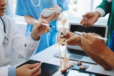 Tıbbi ekip, beyaz laboratuvar önlüklü ve ameliyat önlüklü doktorlarla toplantı yapıyor. Masada oturuyorlar ve tıp endüstrisinde dijital tablet ve dizüstü bilgisayar kullanıyorlar.