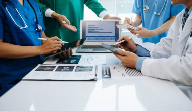 Tıbbi ekip bir masada oturup hastaları tartışıyor, internette çalışıyor ve hastane ya da tıp sektöründe bilgisayar kullanıyor.