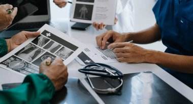 Tıbbi ekip, beyaz laboratuvar önlüklü ve ameliyat önlüklü doktorlarla toplantı yapıyor. Masada oturmuş, internette çalışan hastaları tartışıyorlar. Tıp endüstrisinde bilgisayar kullanıyorlar.