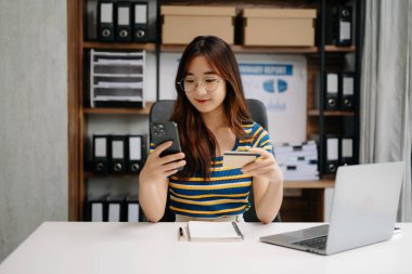 Asyalı genç üniversite öğrencisi kredi kartıyla online alışveriş yapıyor. 