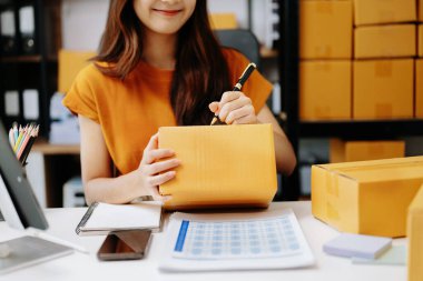 Genç Asyalı iş kadını, paket kutusu hazırla ve çevrimiçi alışveriş konseptine çevrimiçi teslimat için online siparişleri kontrol et.