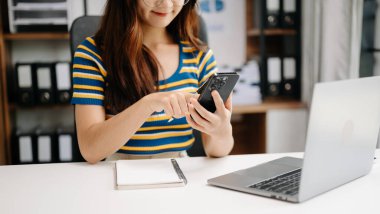 İş kadını eli dizüstü bilgisayarla çalışıyor ve not defterine notlar alıyor.