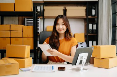 Başlangıçta küçük işletme KOBİ 'si, Asyalı kadın girişimci çevrimiçi siparişleri kontrol ediyor ve nakliye için paketler hazırlıyor