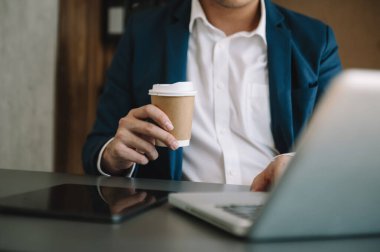 Adam dizüstü bilgisayar kullanıyor ve dizüstü bilgisayarda daktilo kullanıyor ve kahve fincanı tutuyor.