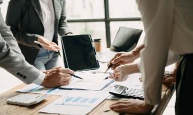 Ofis masasında, ofisteki tabletle birlikte laptopun maketini kullanan ve ona bakan insanlar.