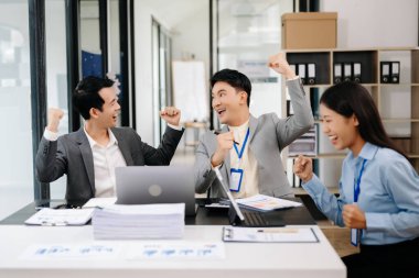 Bir grup Asyalı genç iş adamı modern ofiste elde ettikleri başarıyı kutluyor.