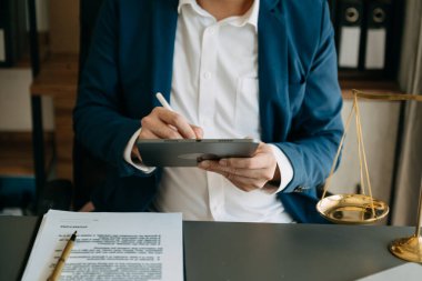 Adalet ve hukuk kavramı. Tahta masadaki dijital tablet bilgisayarla çalışan tokmak, mahkeme salonunda bir erkek yargıç.