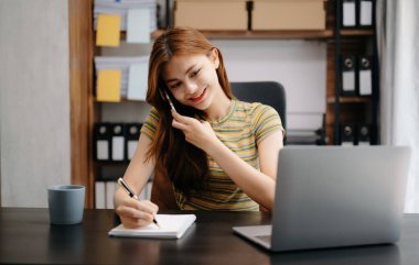 Modern ofiste otururken telefonda konuşan Asyalı bir iş kadını.