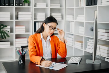 Çekici Asyalı kadın ofis çalışanı takım elbise modern ofiste bilgisayarla çalışıyor.