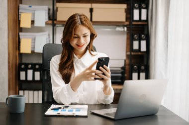 Kendine güvenen iş uzmanı yaratıcı ofiste akıllı telefonu masanın üstünde tutuyor.