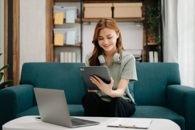 Kanepede oturan kız öğrenci, oturma odasındaki online bilgileri aramak için tablet bilgisayar kullanıyor.