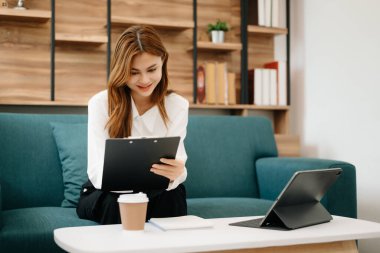 Oturma odasında çalışma odasında, merkez ofisteki kanepede otururken tablet kullanan güzel bir kadın.