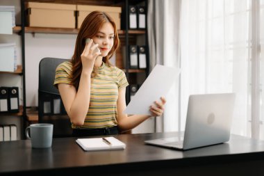 Modern ofiste otururken telefonda konuşan Asyalı bir iş kadını.