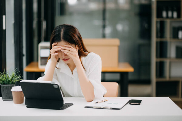 Азиатская деловая женщина напряжена и скучает после долгого дня в офисе.