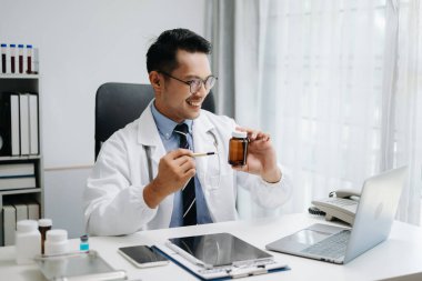 Bilgisayarla çalışan, beyaz üniformalı, kendinden emin genç bir erkek doktor.