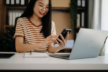 İş kadını sabah ışığında ofis masasında akıllı telefon ve laptop kullanıyor.