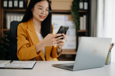 İş kadını sabah ışığında ofis masasında akıllı telefon ve laptop kullanıyor.