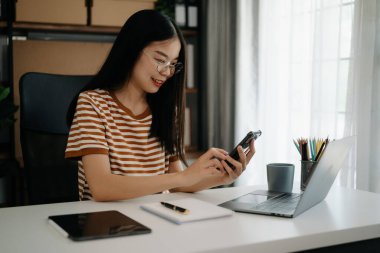 İş kadını sabah ışığında ofis masasında akıllı telefon ve laptop kullanıyor.