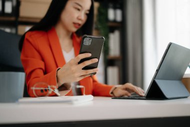 İş kadını sabah ışığında ofis masasında akıllı telefon ve laptop kullanıyor.