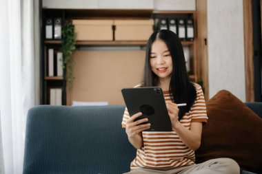 Evdeki kanepede dijital tablet kullanan Asyalı kadın.