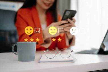 Müşteri hizmetleri değerlendirme konsepti. İş kadını, akıllı telefondaki sanal ekranda gülümseyen yüz ifadesine basıyor.