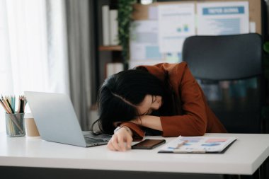 Asyalı kadın migren ağrısı çekiyor. Ofiste dizüstü bilgisayarla çalışan aşırı çalışan iş kadını finansör.