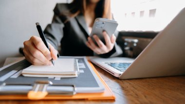 İş kadını sabah vakti ofisteki masada akıllı telefon üzerinde çalışıyor.