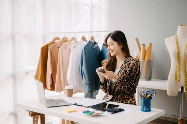 Asyalı terzi kadın terzi atölyesinde kıyafetlerle çalışıyor. Stüdyoda güzel genç bayan moda tasarımcısı
