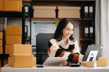Küçük işletme KOBİ 'si kurun. Dijital tablet kullanan Asyalı kadın, paket ürün kutusu hazırlamak için online alışveriş siparişi alıyor ve kontrol ediyor.