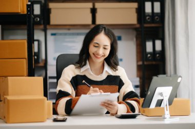 Güzel Asyalı bayan blogcu dijital tablette video kaydına kamera önünde kıyafetlerini gösteriyor, dükkanında canlı yayın yapıyor. Çevrimiçi Alışveriş Arabası kavramı
