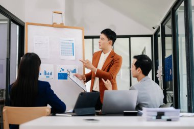 Patron grafiklerle kurulun yanında duruyor, istatistikleri gösteriyor, eğitime katılan çeşitli personel, şirketin yeni ürünlerini ofiste tanıtıyor.