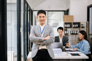 Modern ofisteki kameraya gülümseyen takım elbiseli yakışıklı Asyalı erkek ofis çalışanı.