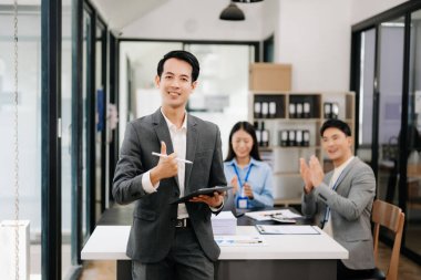 Modern ofisteki kameraya gülümseyen takım elbiseli yakışıklı Asyalı erkek ofis çalışanı.
