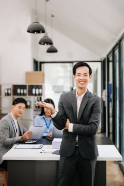 Modern ofisteki kameraya gülümseyen takım elbiseli yakışıklı Asyalı erkek ofis çalışanı.