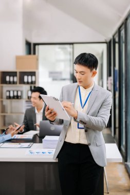 Modern ofisteki kameraya gülümseyen takım elbiseli yakışıklı Asyalı erkek ofis çalışanı.