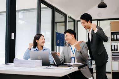 Genç Asyalı iş adamlarından oluşan bir grup, modern ofiste başarıyı ve tasarım tasarımını kutluyor.