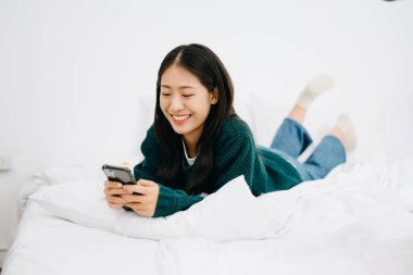 Beyaz bir yatakta akıllı telefon kullanan güzel bir genç kadın, yaşam tarzı konsepti.